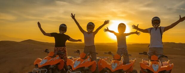 Group of friends enjoying a quad biking tour at sunset in the Agafay Desert near Marrakech, riding orange ATVs with arms raised in celebration against a golden sky.