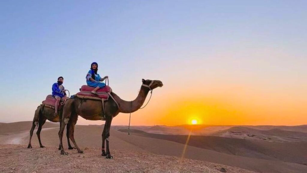Couple enjoying a camel ride adventure at sunset in the Agafay Desert near Marrakech, Morocco.