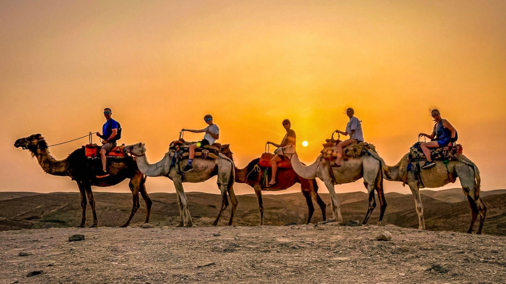 Tourists enjoying a camel ride at sunset in the Agafay Desert near Marrakech, Morocco.