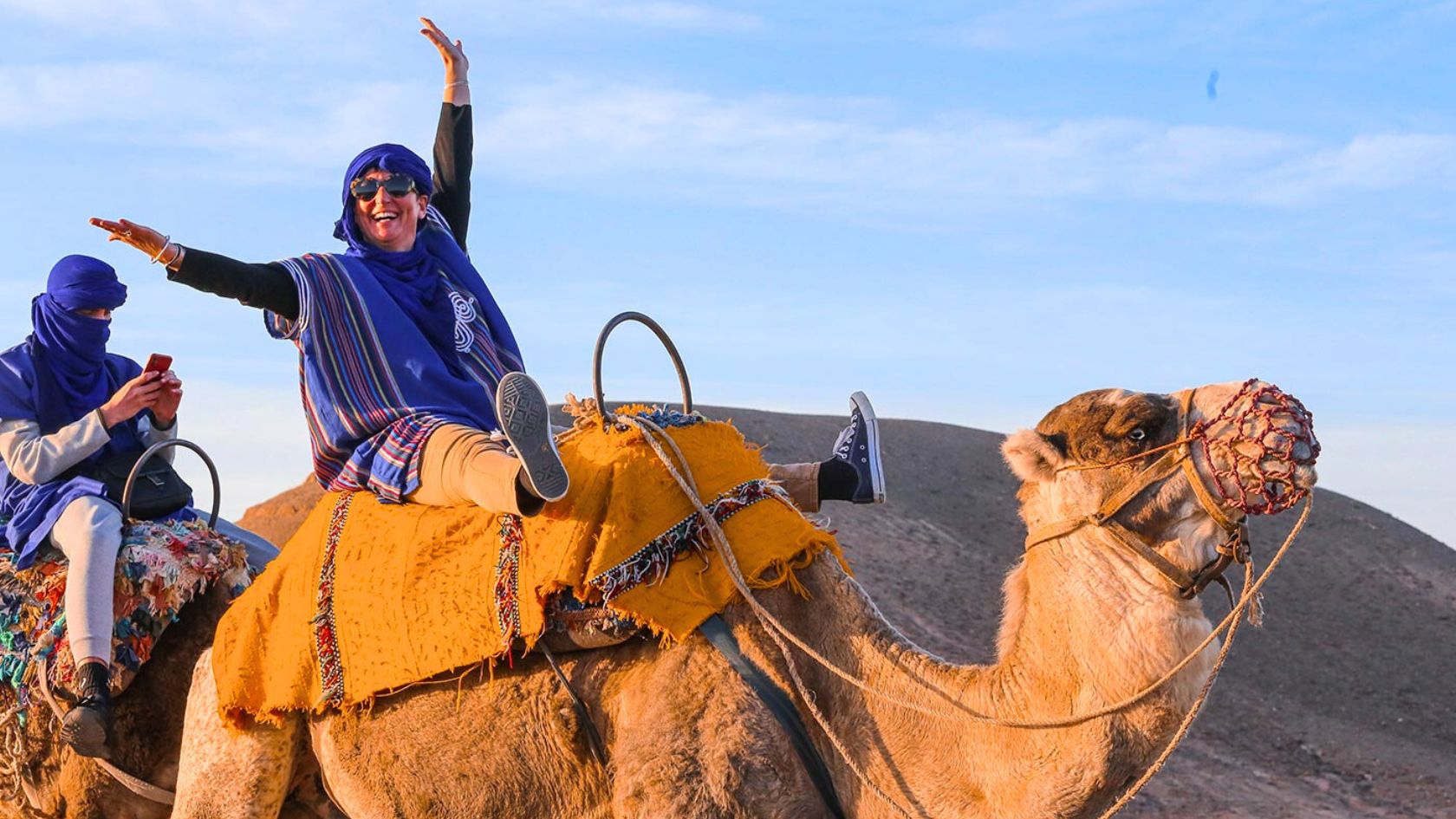 Happy travelers enjoying a family camel ride adventure in the Agafay Desert near Marrakech under a clear blue sky.